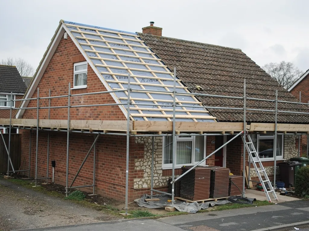 A 1970s semi-detached house mid re-roof, half stripped to new battens and breathable membrane, scaffold around it
